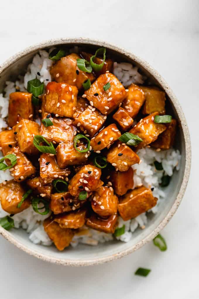 A bowl filled with rice and sweet and sour tofu topped with sliced green onions