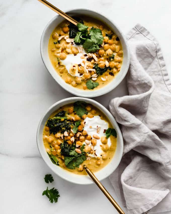 Two bowls of coconut chickpea curry with a grey napkin on the side