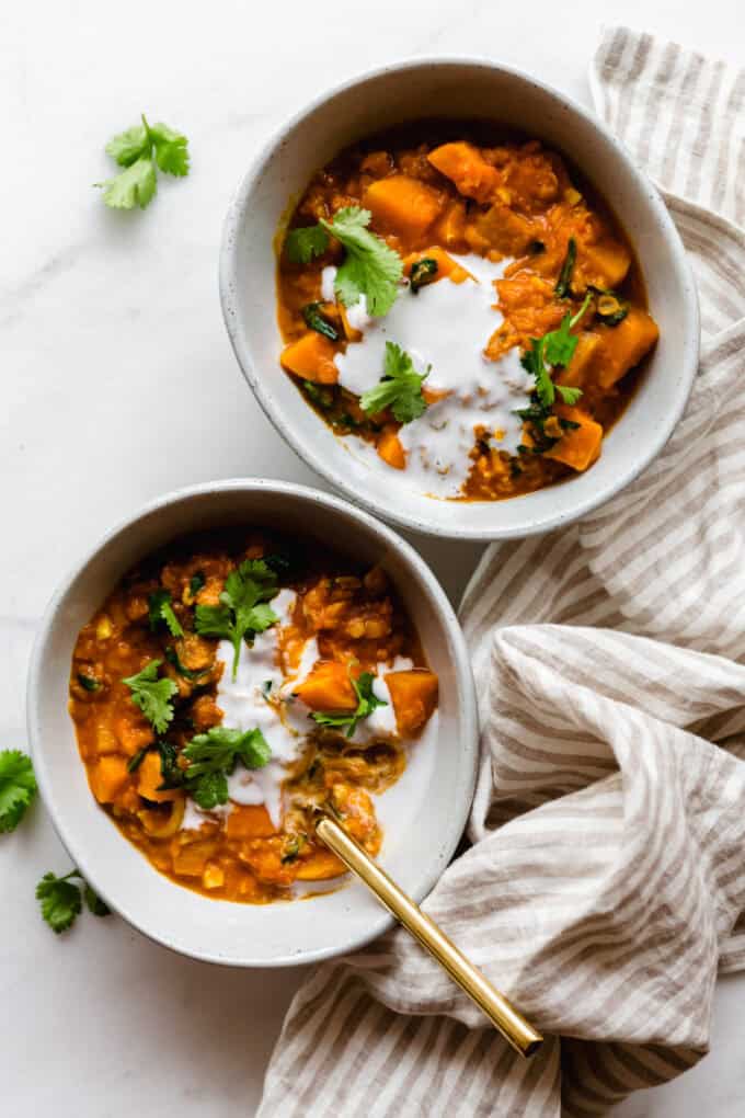 two bowls of sweet potato lentil curry topped with coconut milk and cilantro