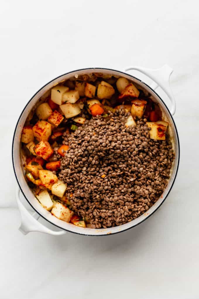 A white pot with brown lentils and potatoes in it