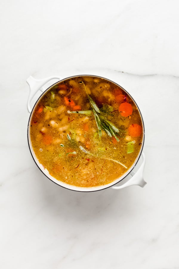 A white pot filled with veggies and soup broth