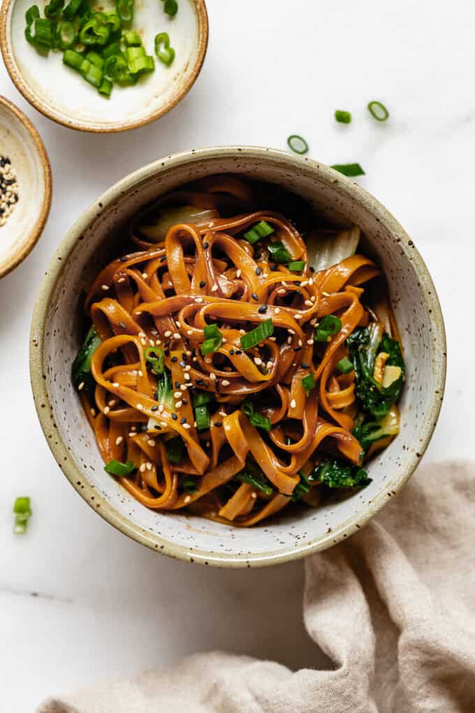 a bowl of miso noodles and bok choy topped with scallions and sesame seeds