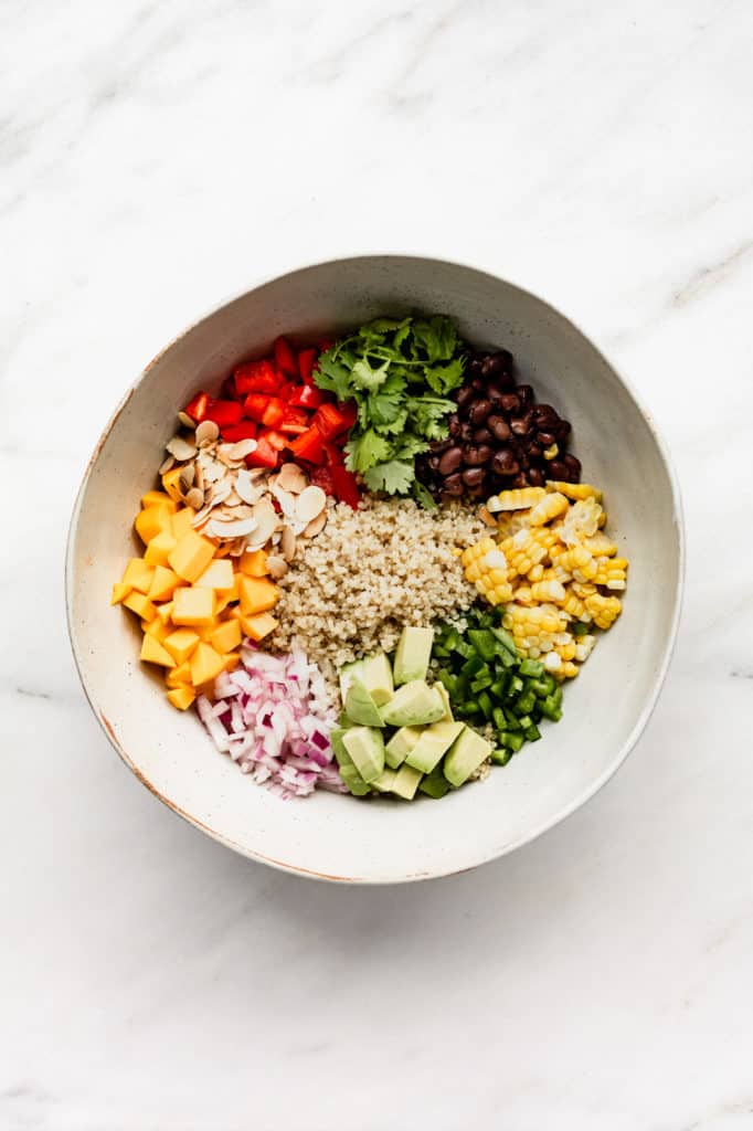 A large mixing bowl with quinoa, black beans, corn, avocado, jalapeno, red onions, mango, almonds, red pepper and cilantro in it