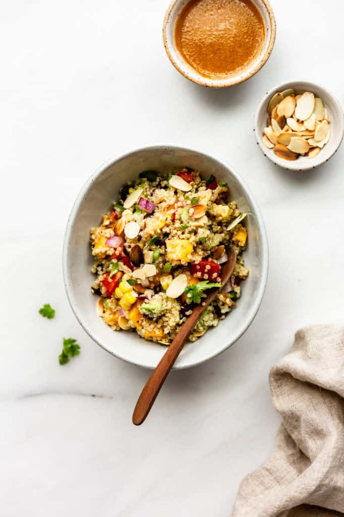 A bowl of southwest quinoa salad with two small bowls of salad dressing and toasted almonds on the side