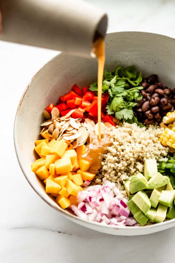 Salad dressing being poured into a bowl of quinoa salad